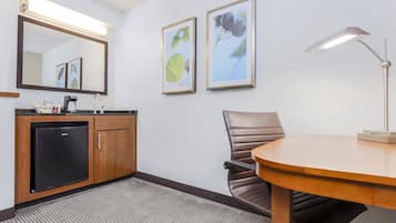A hotel room with a wooden desk, a chair, a black refrigerator, a sink, and two framed pictures on the wall.