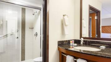 A hotel bathroom with a glass-enclosed shower, a sink with a marble countertop, and a large mirror.
