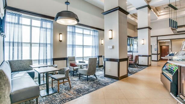 Un hall d’hôtel doté d’un espace salon, d’un coin café et de grandes fenêtres.