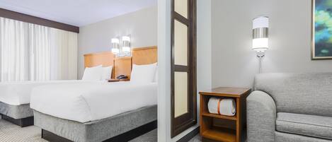 Quarto de hotel com duas camas, um sofá, uma mesinha de cabeceira e um quadro na parede.