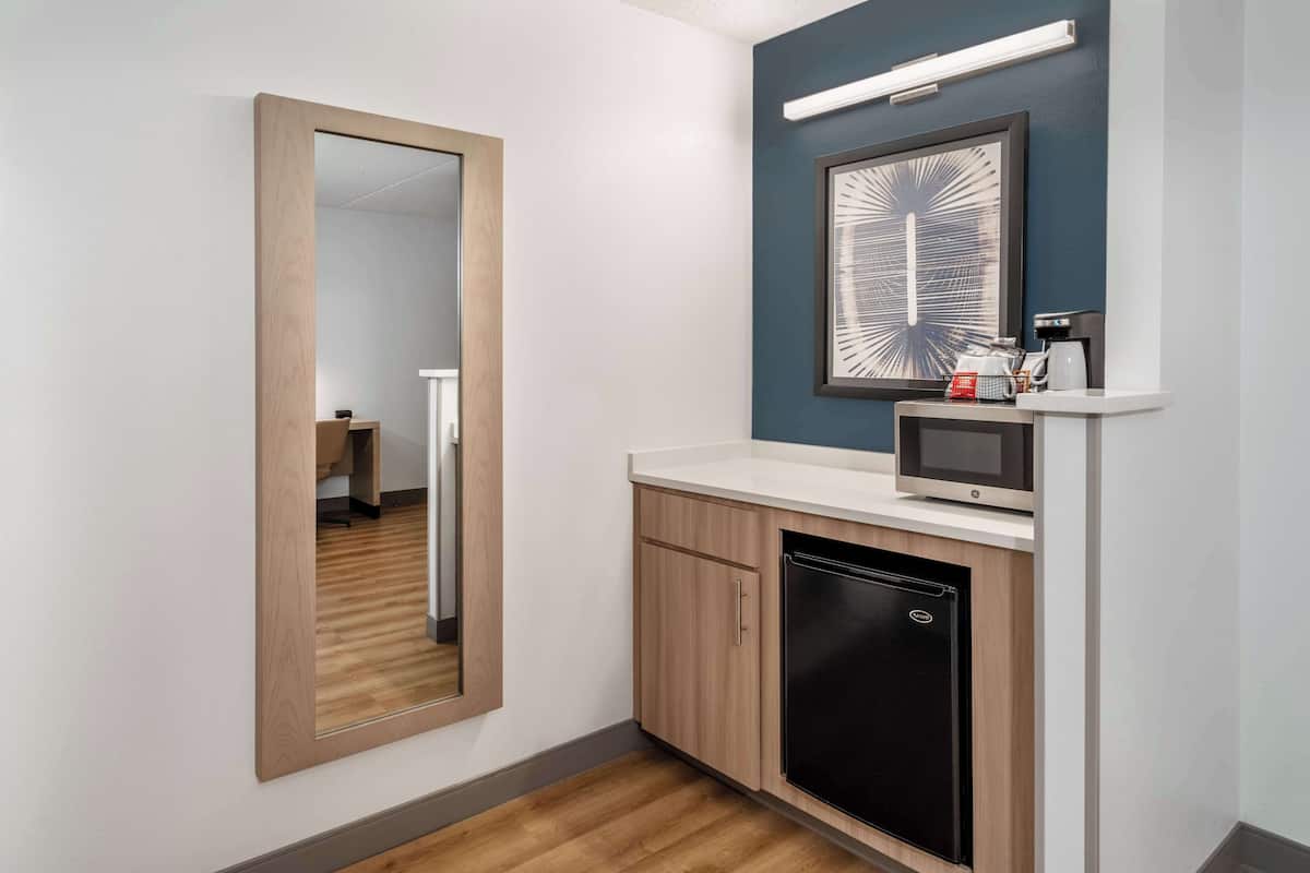 Une salle de bain moderne avec un meuble en bois, un réfrigérateur noir, un four à micro-ondes et une œuvre d’art encadrée accrochée au mur.