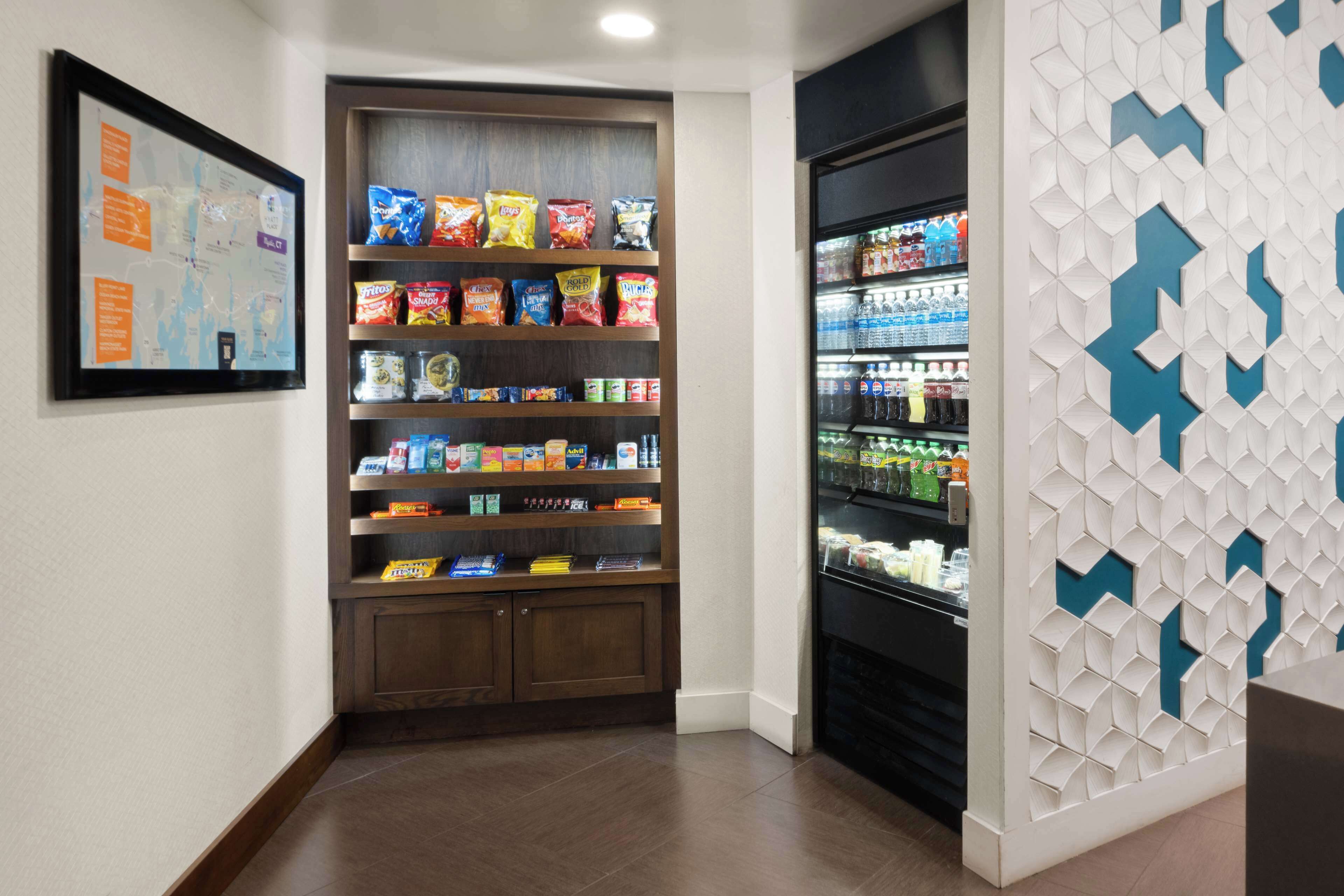 Un rincón del vestíbulo de un hotel con un estante de aperitivos repleto de alimentos envaselados y una vitrina refrigerada.