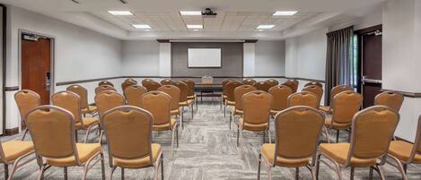 A conference room with rows of chairs, a projector screen, and a carpeted floor.