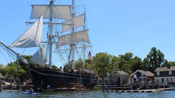 A tall ship docked at a pier with a small docked boat nearby.