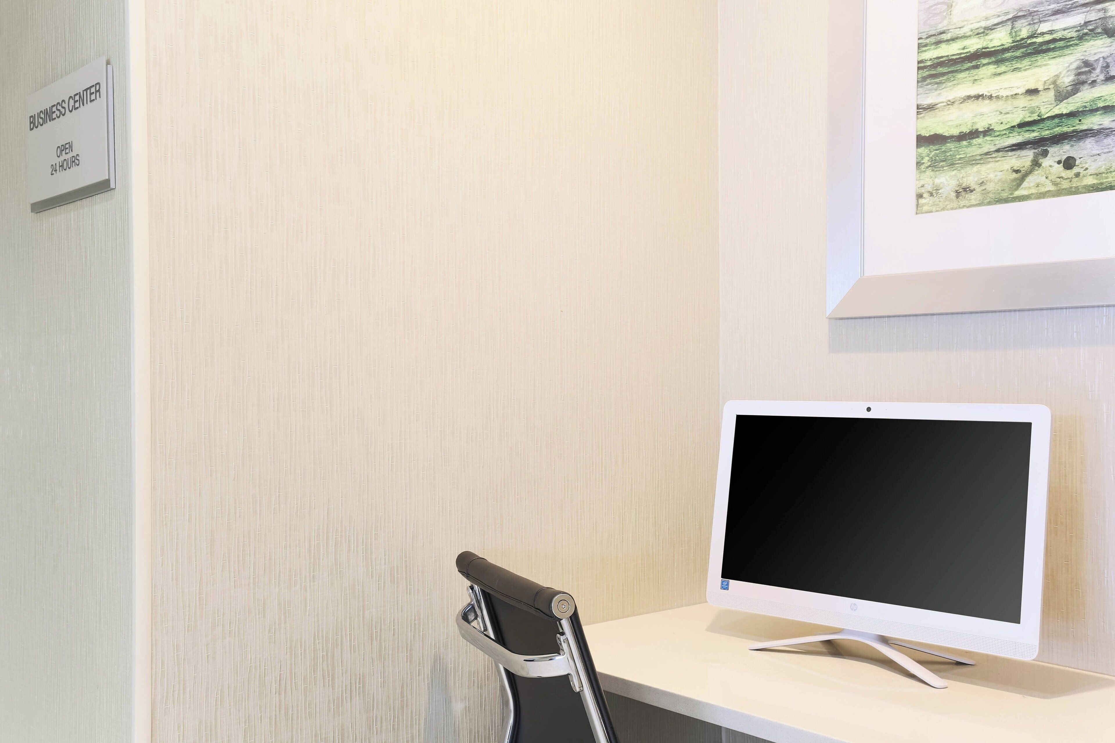Een businesscenter met een bord dat 24 uur aangeeft, een bureau met een computerscherm en een stoel.