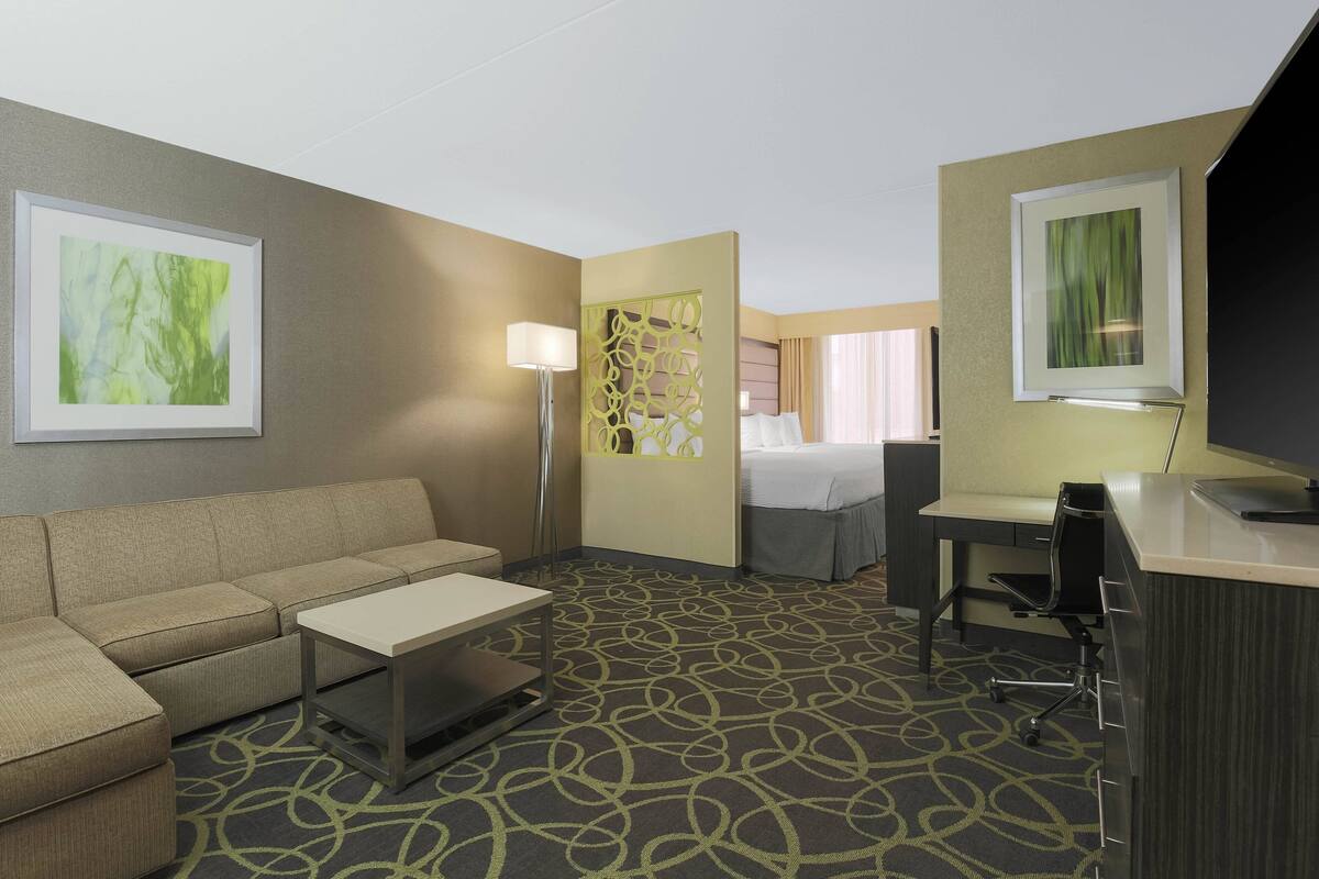 A hotel room with a sofa, a desk, a chair, a bed, and two wall-mounted lamps.
