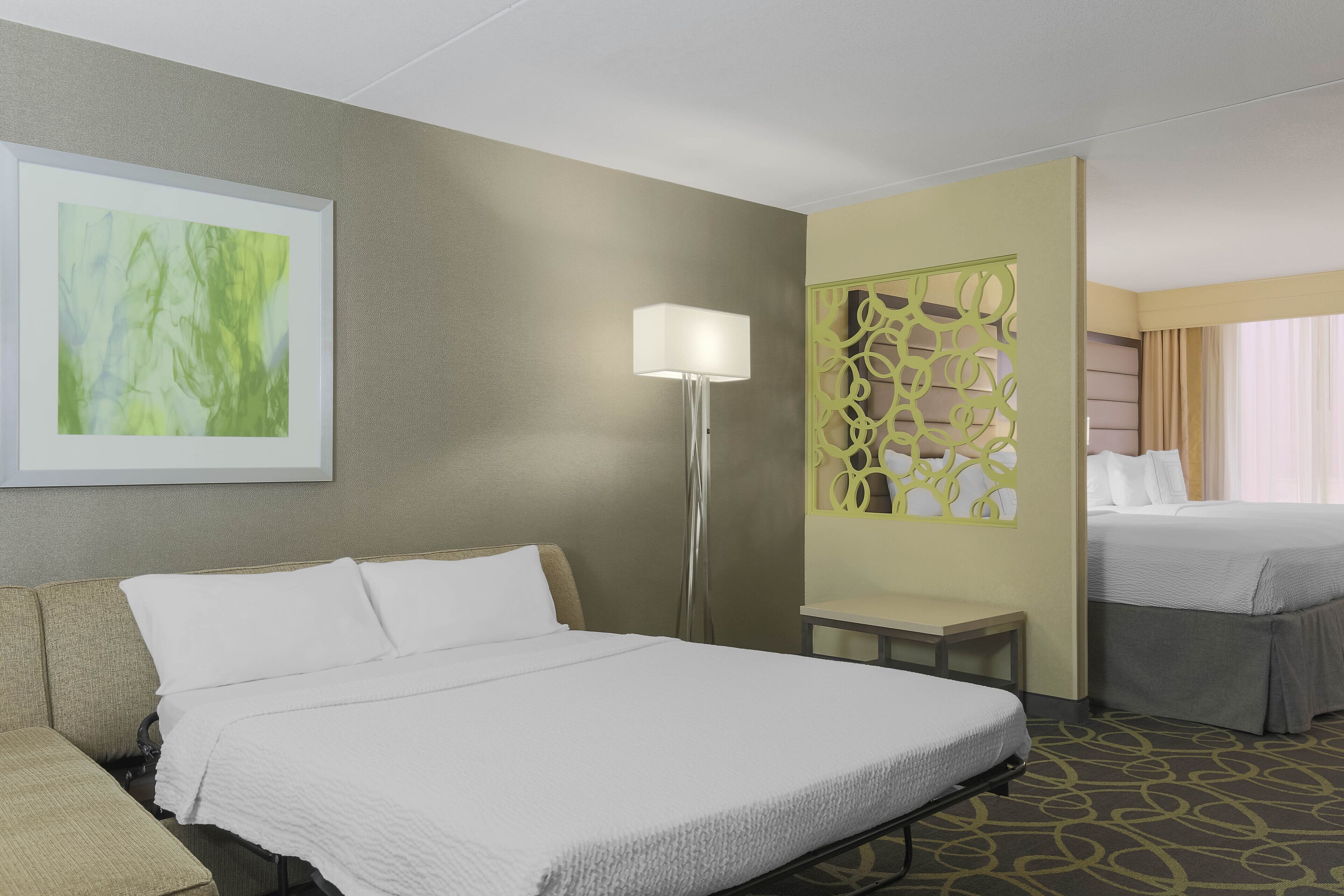 Una habitación de hotel con una cama grande, una mesita de noche, una lámpara de pie y un separador decorativo.