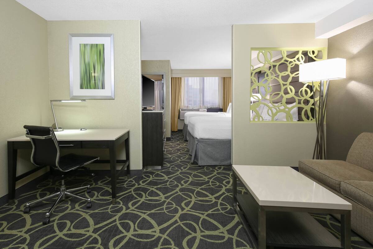 A hotel room with a desk, chair, bed, and a sofa.