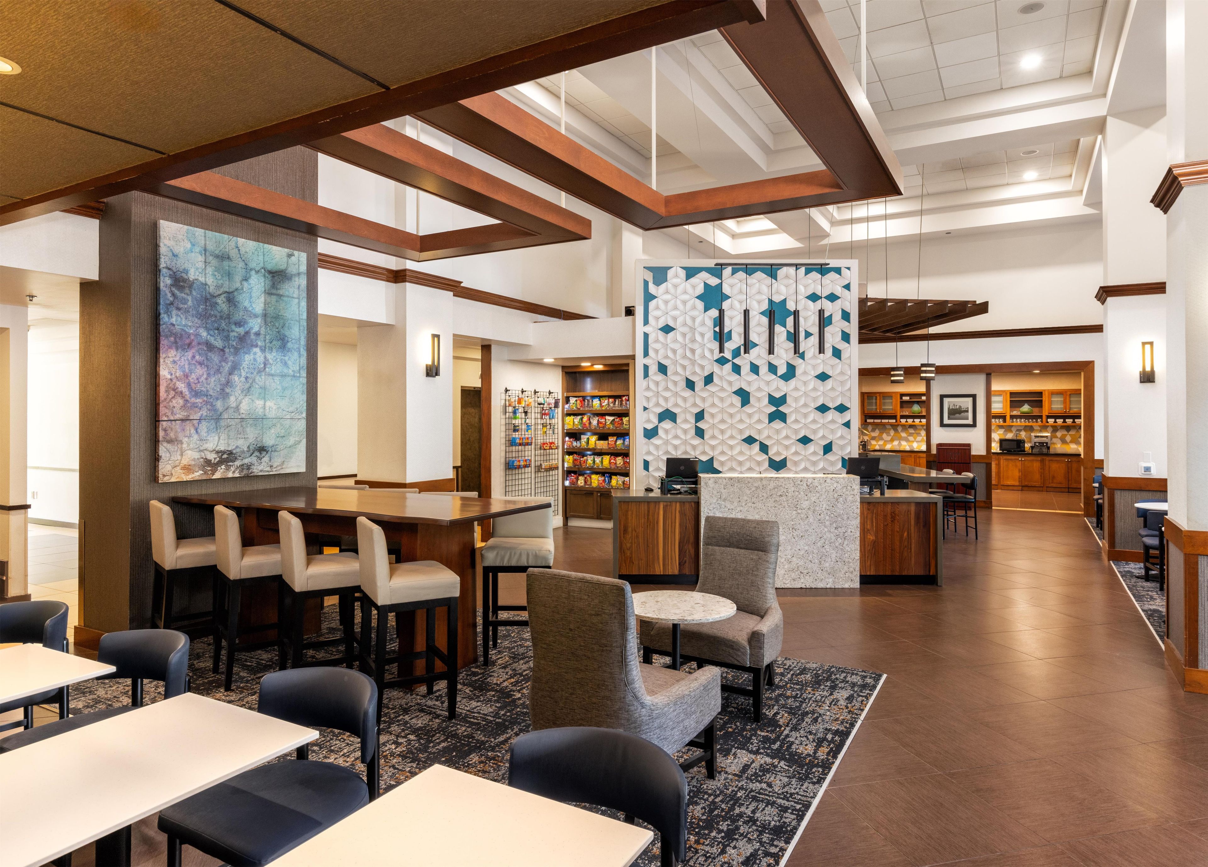 A hotel lobby with a bar area, seating arrangements, and a kitchen in the background.