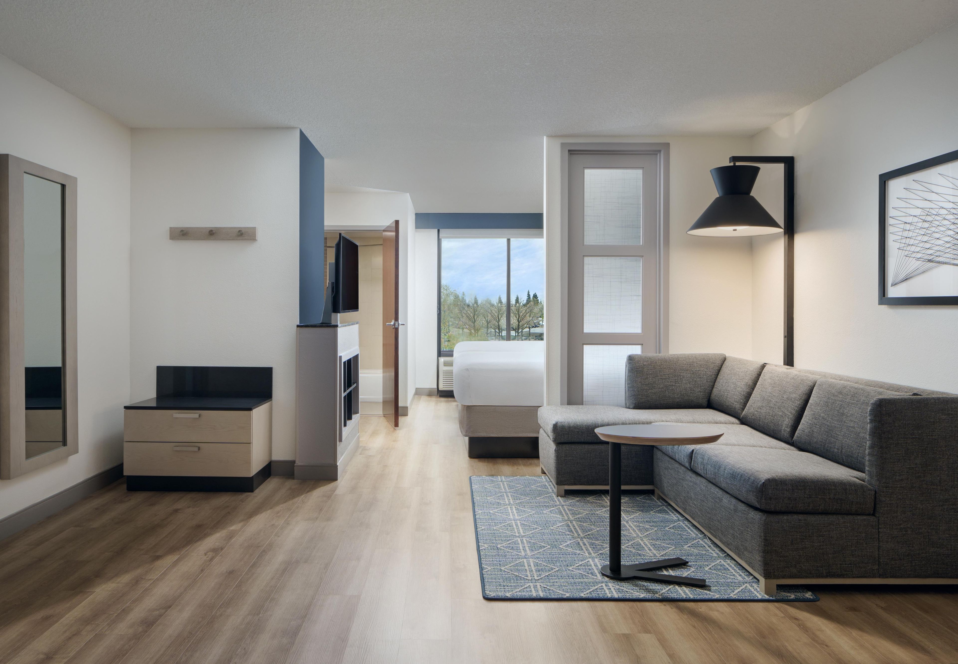 A modern interior with a sofa, a small table, a lamp, and a view through a window.