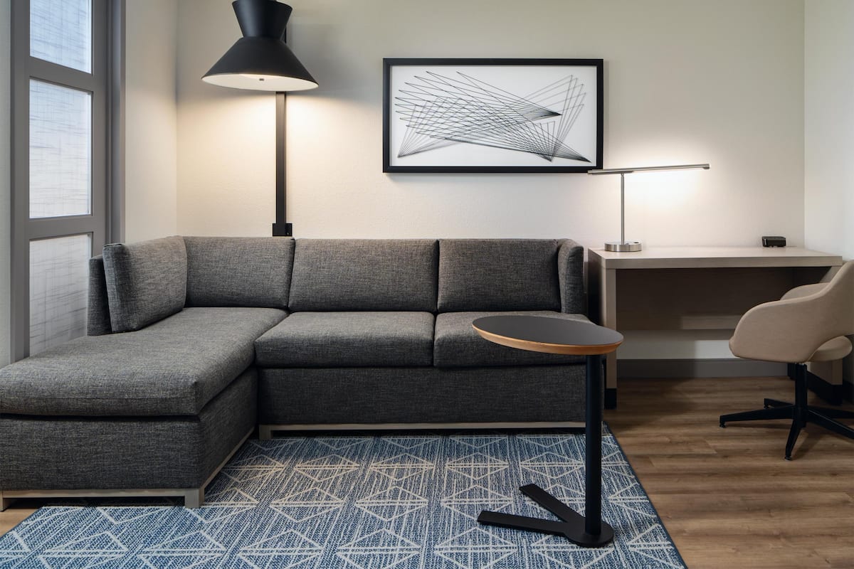 A modern living room with a gray sectional sofa, a round coffee table, a floor lamp, a framed abstract artwork, and a small side table.