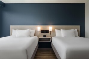 A hotel room with two beds, a nightstand, and a wall-mounted lamp.