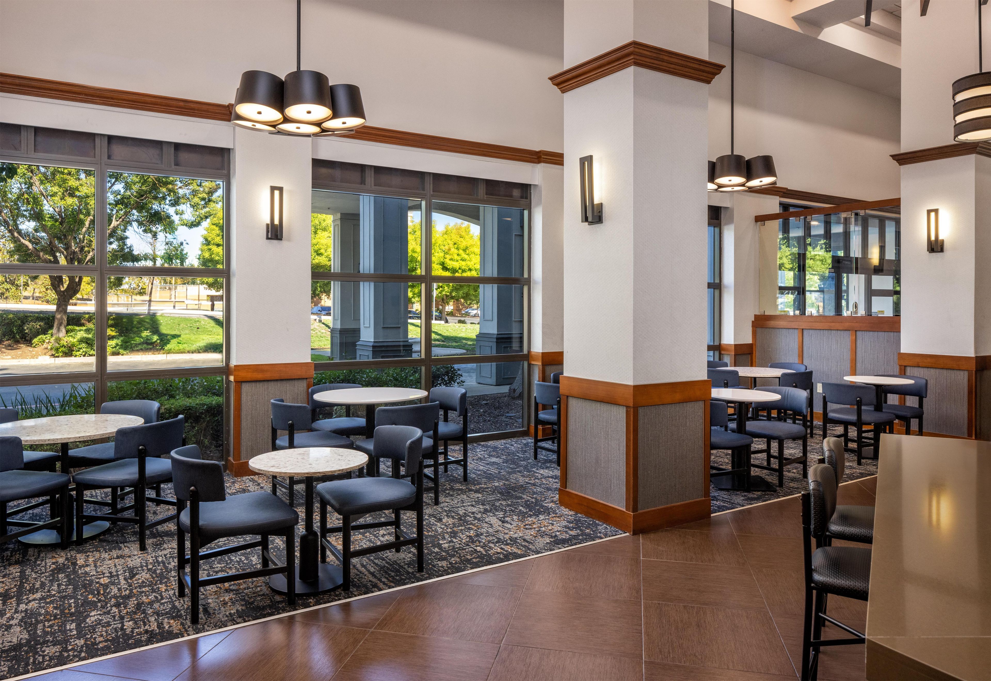 A hotel lobby with multiple seating areas, large windows, and modern lighting fixtures.