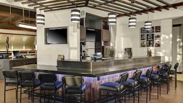 Uma área de bar com ilha central, banquetas, televisão de tela plana e um quadro de menu.