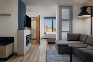 Habitación de hotel moderna con sofá, una mesita redonda, televisor y ventana con vistas a edificios.