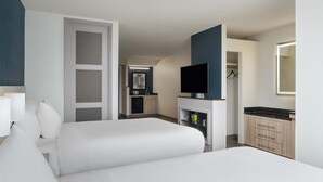 A hotel room with two beds, a TV, a wardrobe, and a small kitchenette.