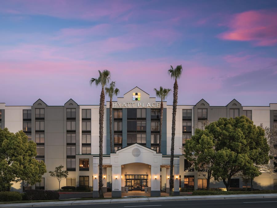 A multi-story hotel with a prominent entrance, palm trees, and a clear sky.