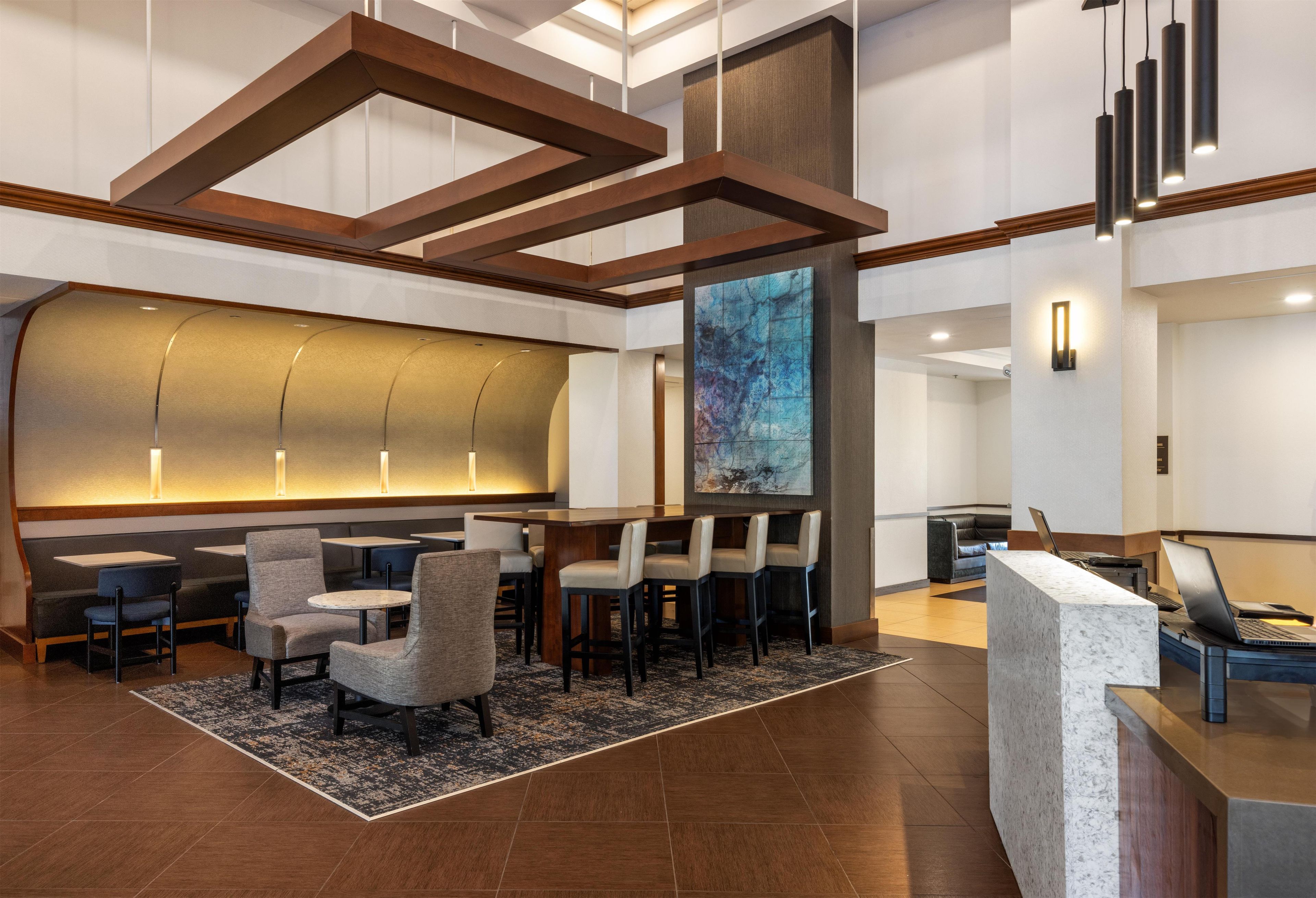 A modern hotel lobby with a reception desk, seating area, and a large abstract painting.
