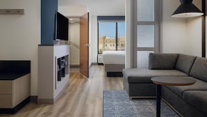 A modern hotel room with a sofa, a small table, a TV, and a window with a city view.