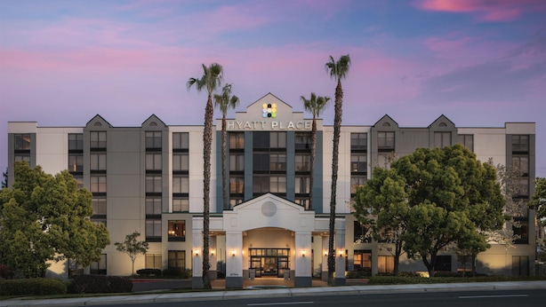 A hotel with a symmetrical facade, a central entrance with a pediment, and palm trees flanking the entrance.