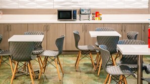 A modern kitchen with a microwave, coffee machine, and various food items on the counter. There are multiple tables and chairs arranged for dining. - Gateway Inn Gardena (Gardena)
