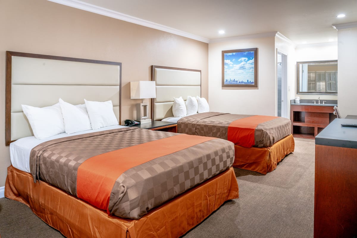 A hotel room with two beds, a desk, a mirror, and a window with a cityscape view.