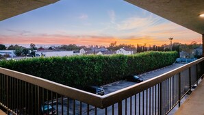 A balcony with a view of a sunset over a residential area, including houses and a hedge. - Gateway Inn Gardena (Gardena)