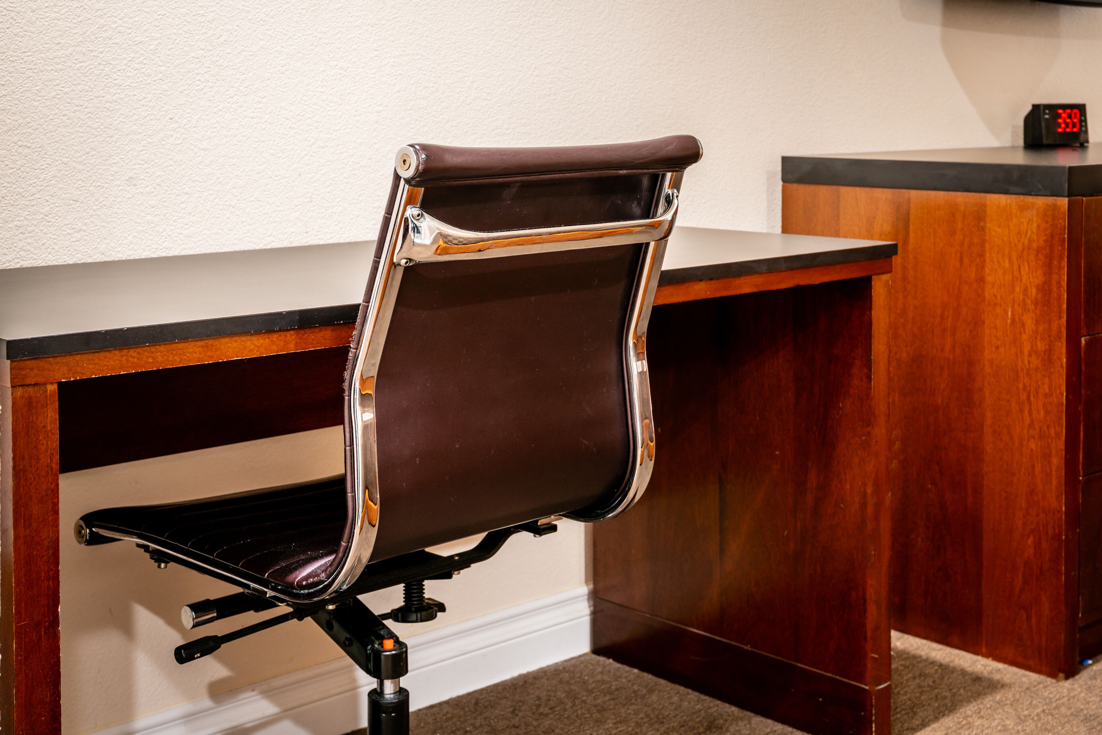 Un fauteuil de bureau moderne, doté d’un haut dossier et d’accoudoirs, placé devant un bureau en bois et un mur blanc.