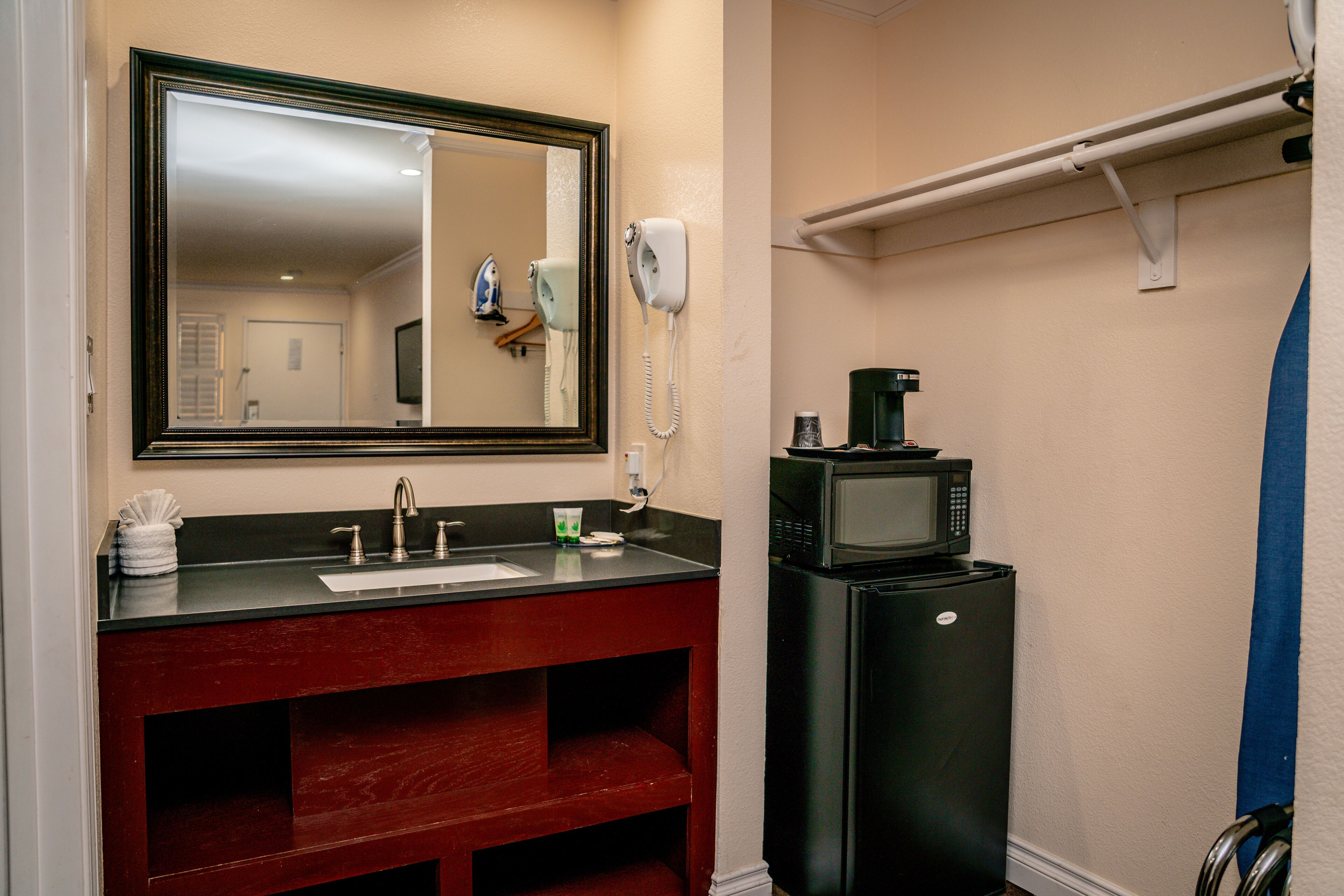 A bathroom with a sink, mirror, hair dryer, and a black refrigerator.