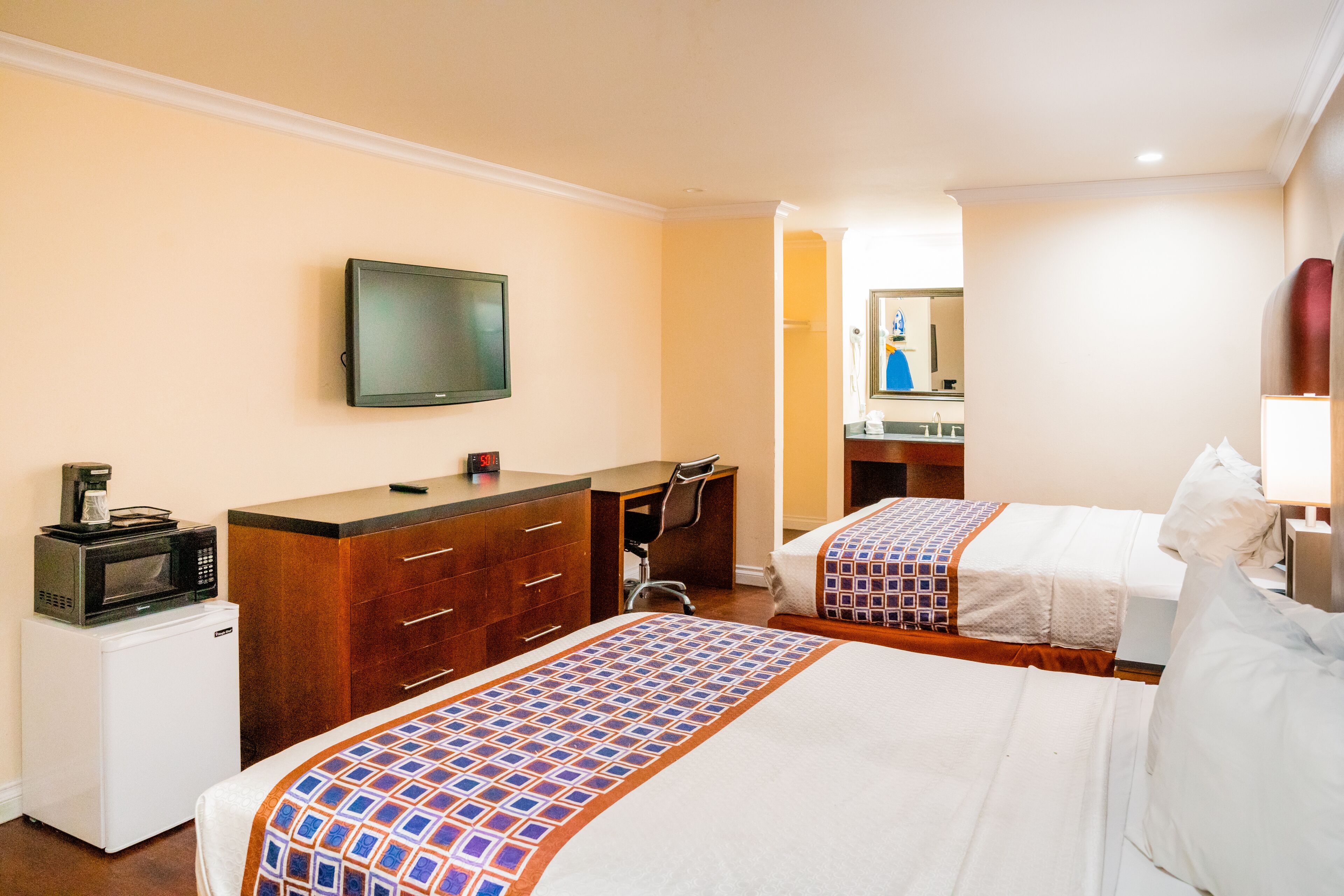 A hotel room with two beds, a desk with a chair, a microwave, and a television on the wall.