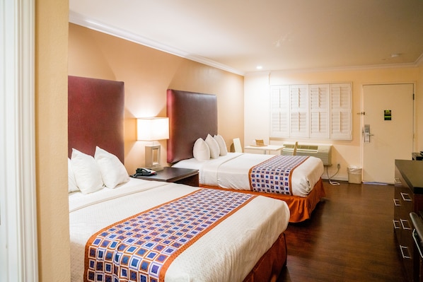 A hotel room with two beds, a desk, and a window with shutters.