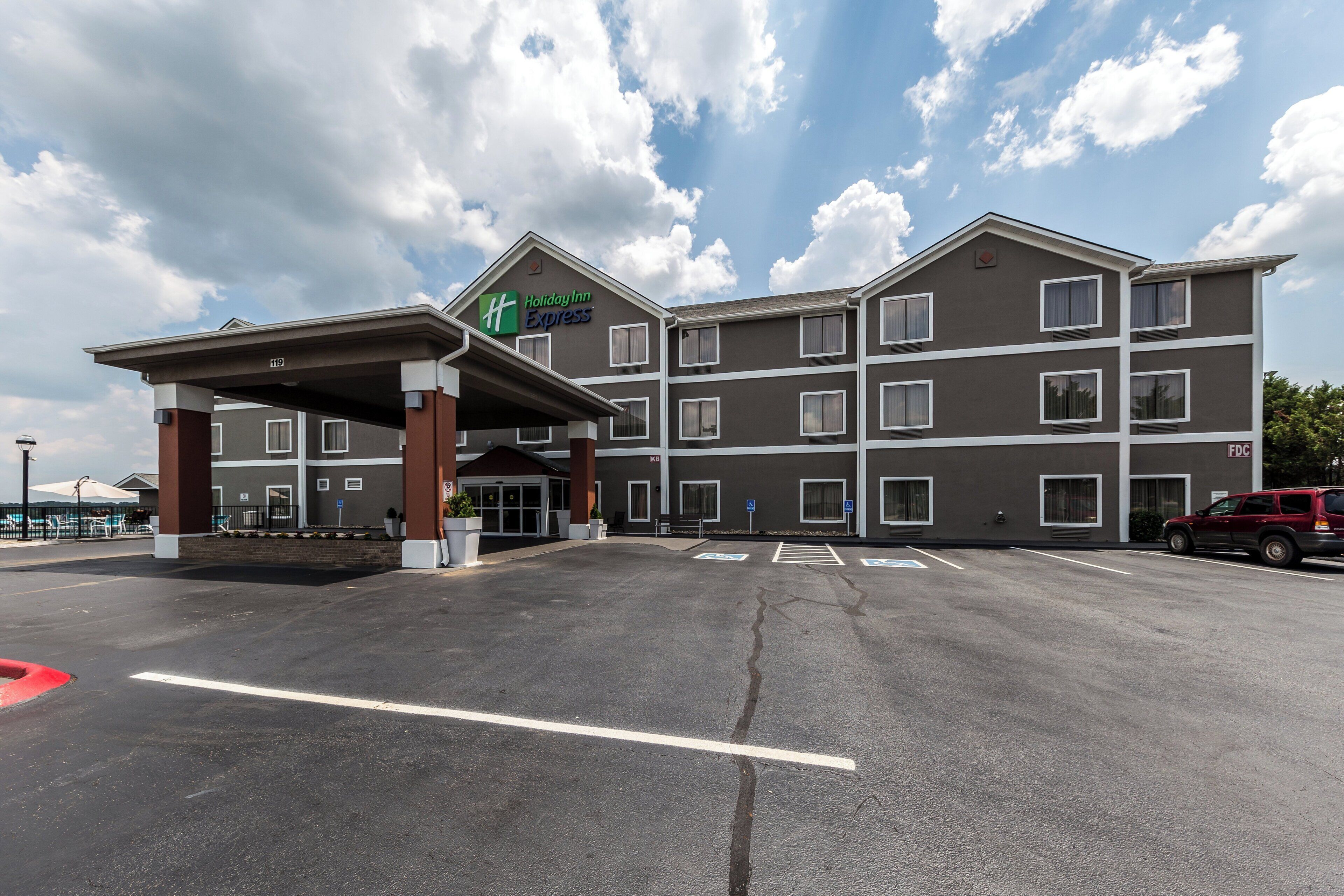 Edifício Holiday Inn Express com entrada coberta, diversas janelas e estacionamento com vagas para deficientes.