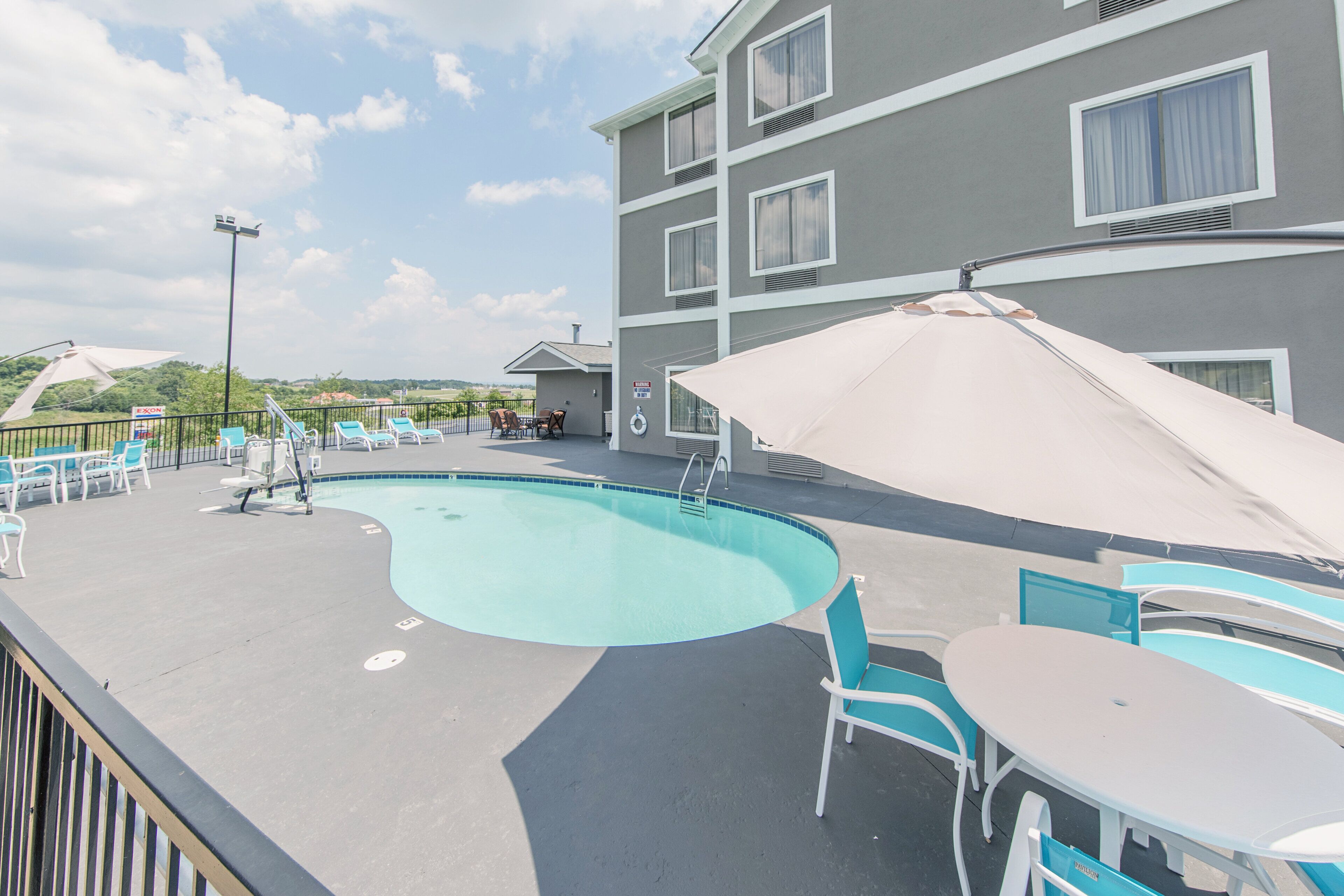 Área de piscina no terraço com espreguiçadeiras e guarda-sóis, piscina e um edifício com várias janelas.