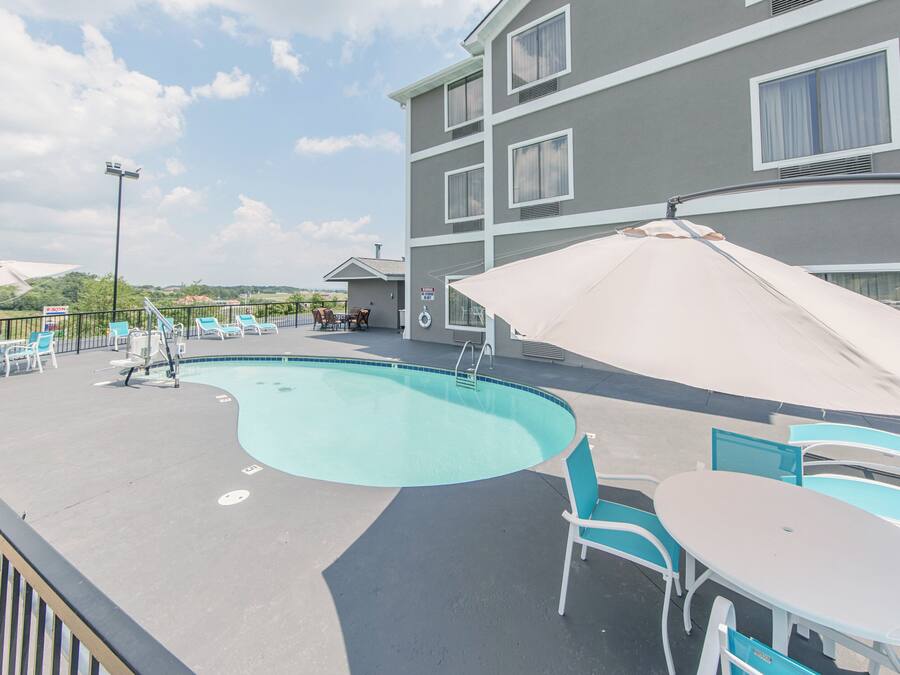 Área de piscina no terraço com espreguiçadeiras e guarda-sóis, piscina e um edifício com várias janelas.