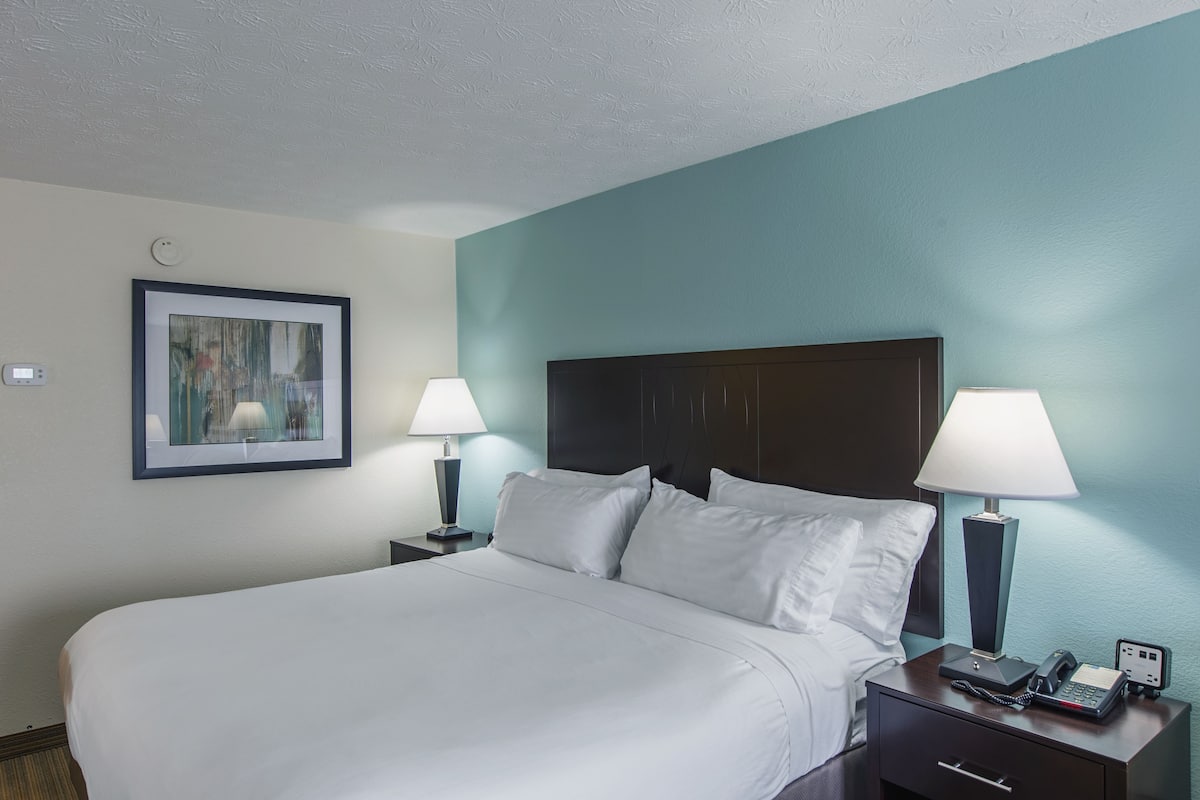 A hotel room with a large bed, two bedside tables with lamps, a framed picture on the wall, and a nightstand with a phone and a power outlet.