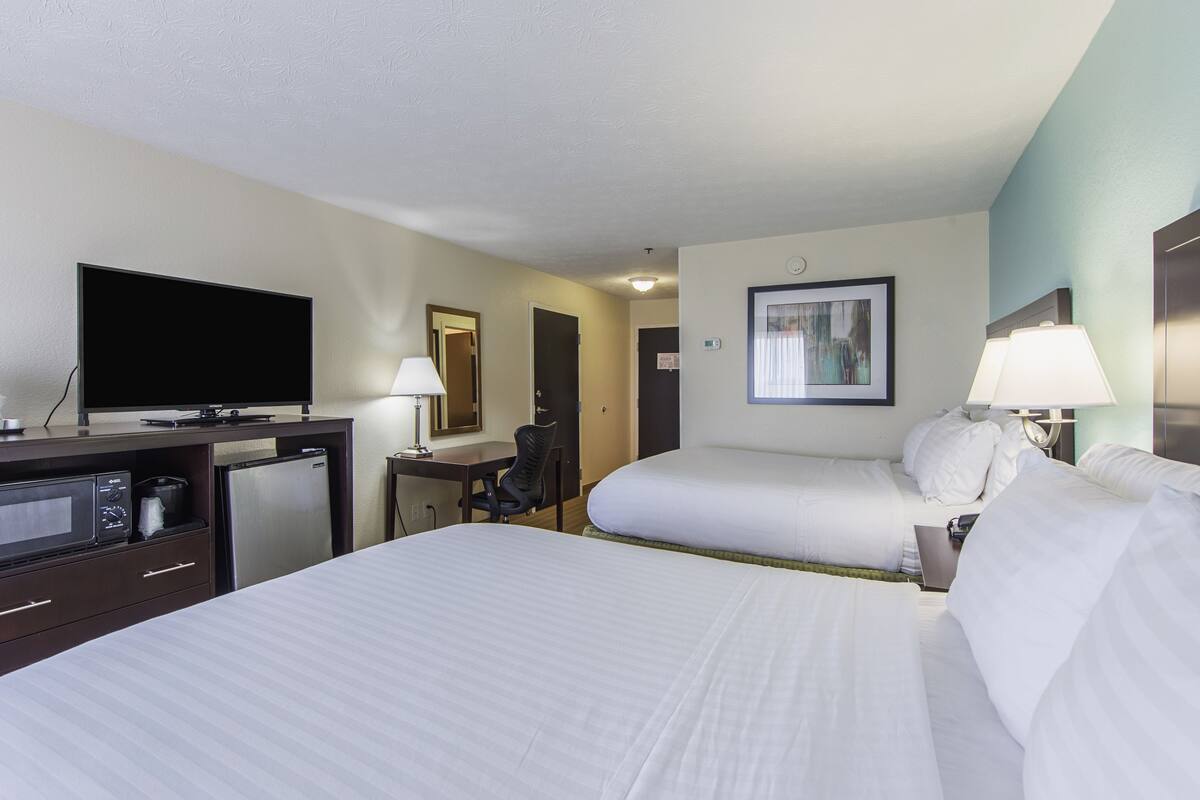 A hotel room with two beds, a desk with a flat-screen TV, a microwave, and a refrigerator.