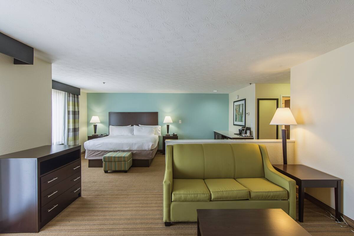 A hotel room with a bed, a green sofa, a desk, a dresser, and two bedside lamps.