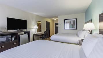 A hotel room with two beds, a desk with a flat-screen TV, a microwave, a refrigerator, and a lamp.