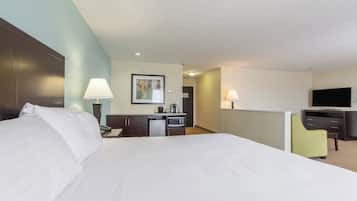 A hotel room with a large bed, a desk with a lamp, a television, and a small kitchenette.
