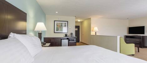 Habitación de hotel con una cama grande, un escritorio con lámpara, televisión y una pequeña cocina.