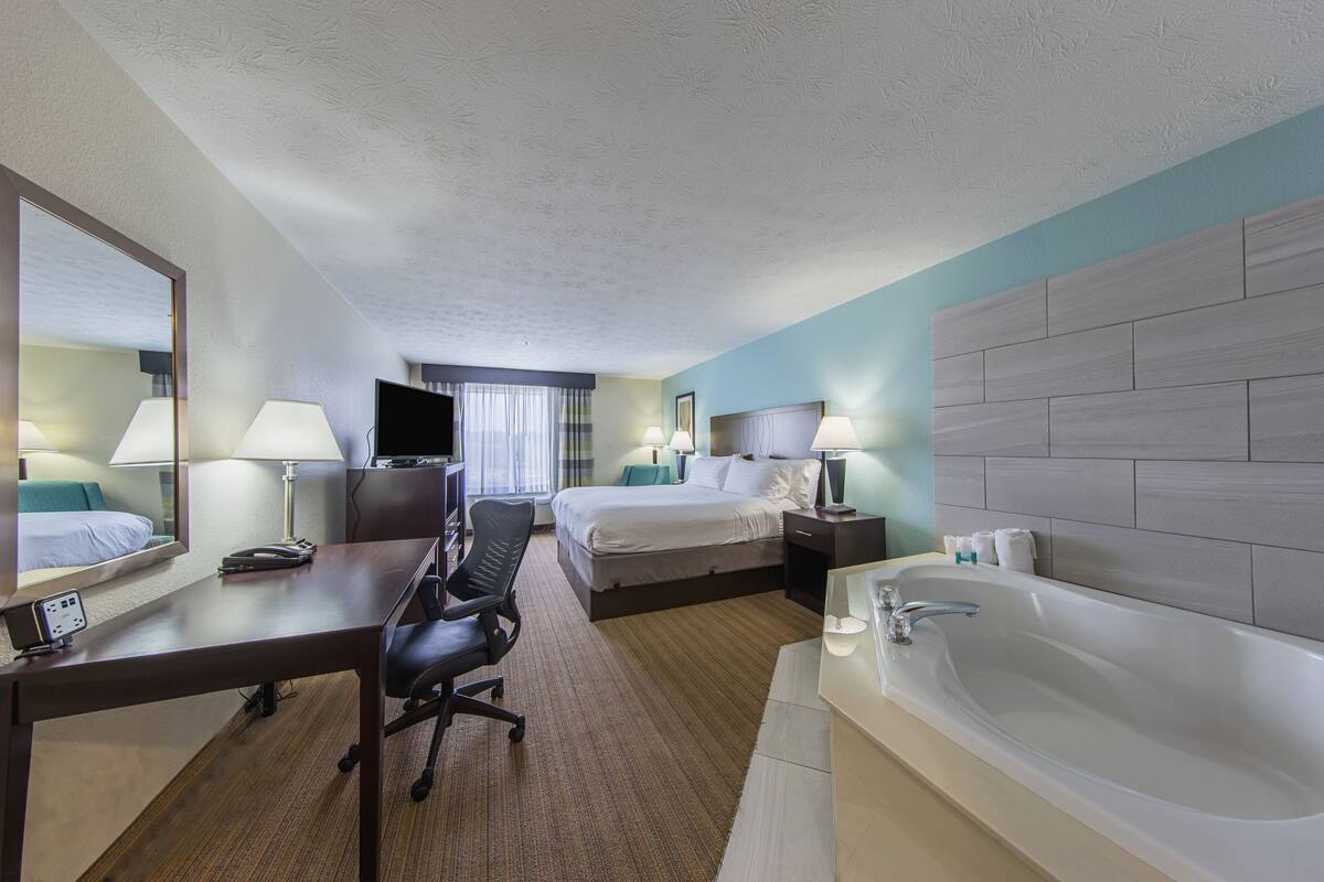 A hotel room with a bed, desk, chair, and a large bathtub.