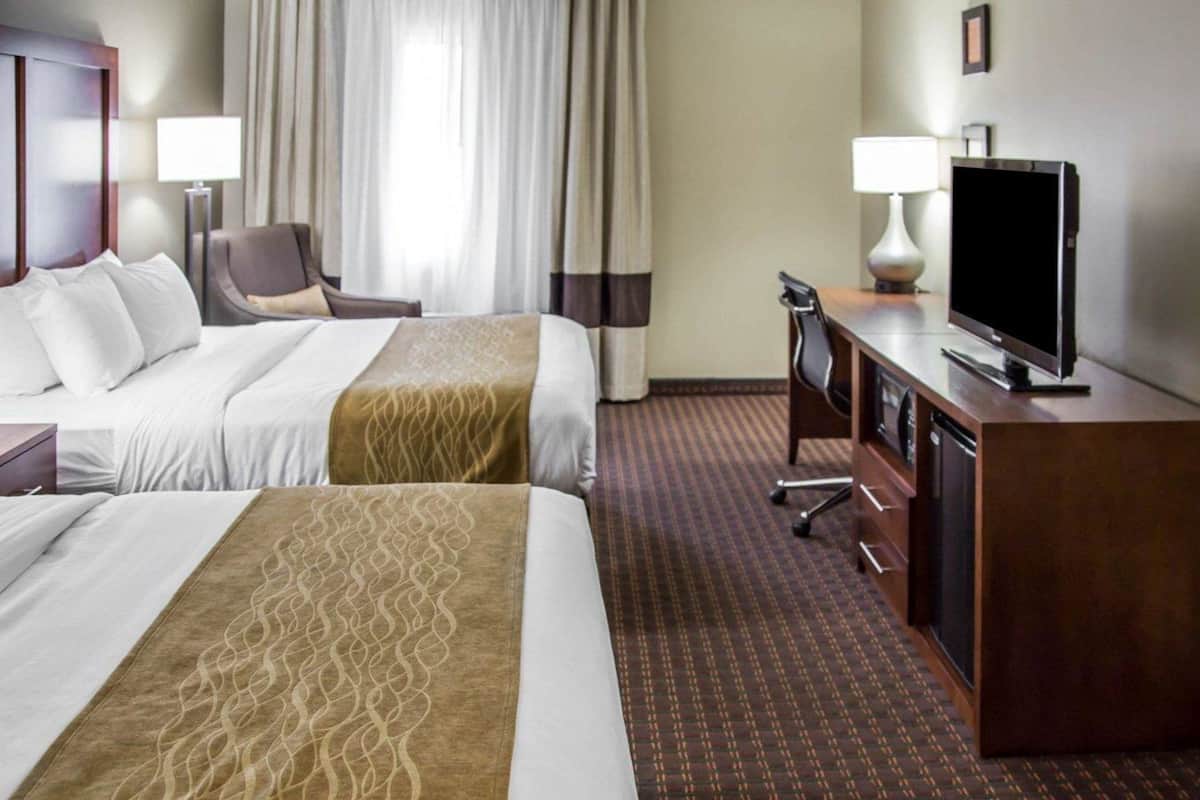 A hotel room with two beds, a desk, a television, and a chair.