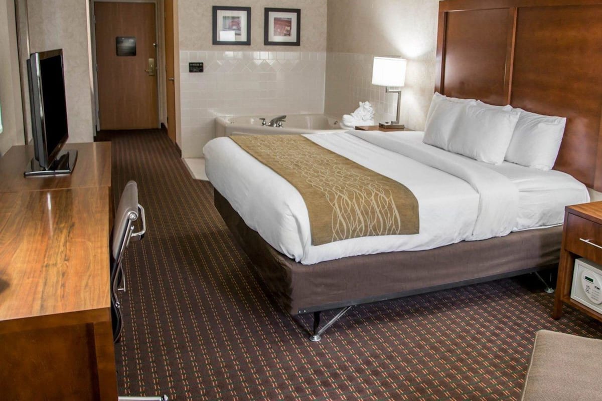 A hotel room with a bed, a desk, a television, a bathroom with a bathtub, and a wall-mounted picture.