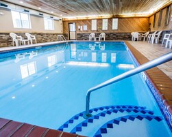 Una piscina interior con superficie de agua azul cristalina, una escalera metálica y un borde de azulejos.