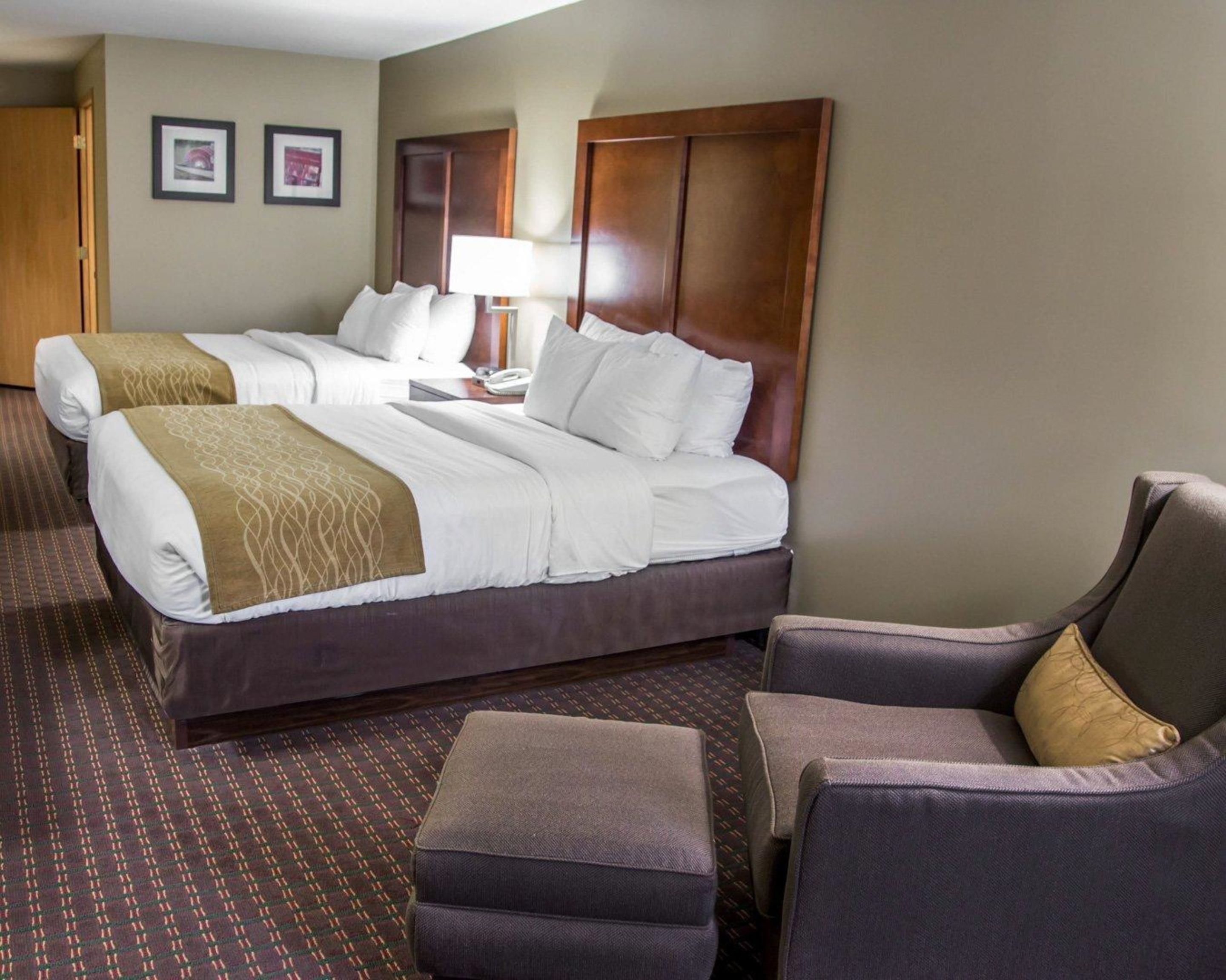 Una habitación de hotel con dos camas, un escritorio, una lámpara y dos sillones.