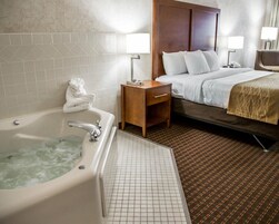 Una habitación de hotel con bañera, cama, mesita de noche y lámpara.