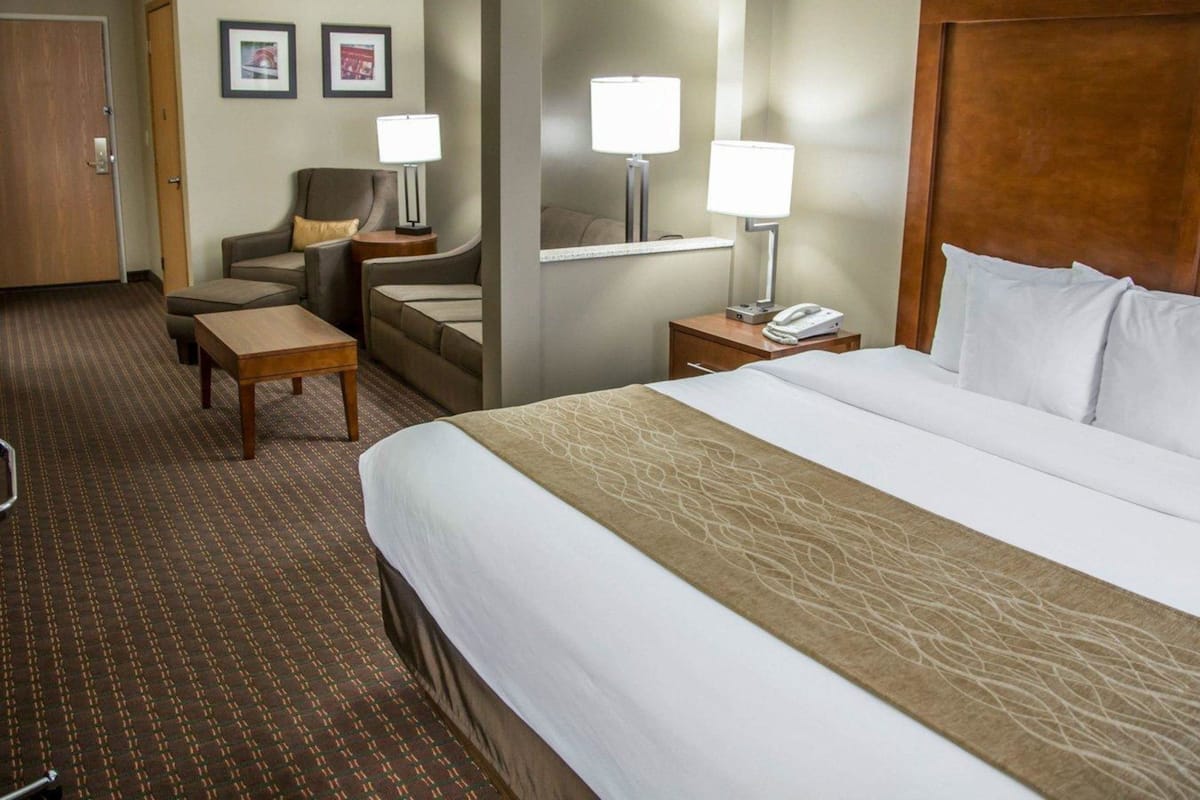 A hotel room with a large bed, a desk, a chair, two bedside lamps, and a telephone.