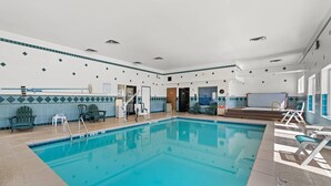 A large indoor swimming pool with clear blue water, surrounded by lounge chairs and a tiled wall with a geometric pattern. - Quality Inn Dodge City (Dodge City)