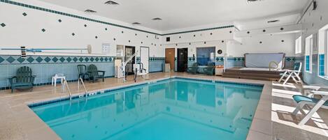 Una amplia piscina interior con agua azul cristalina, rodeada de tumbonas y una pared de azulejos con un diseño geométrico.