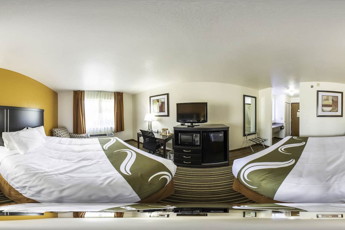 A mirrored hotel room with a bed, a desk, a television, and a microwave.